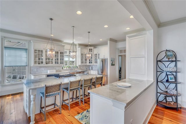 kitchen with stainless steel fridge, a breakfast bar, decorative light fixtures, light hardwood / wood-style floors, and white cabinetry