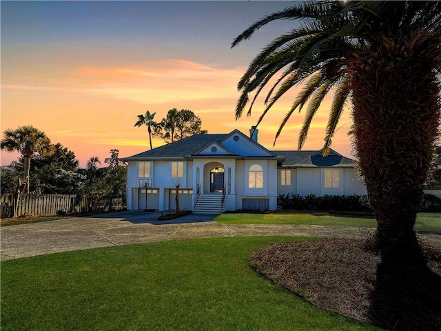 view of front of house featuring driveway, an attached garage, fence, a yard, and stucco siding