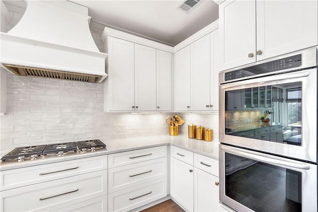 kitchen with backsplash, stainless steel appliances, custom exhaust hood, and white cabinets