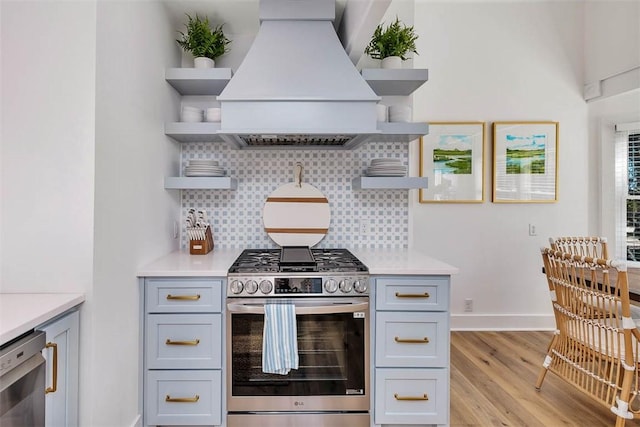 kitchen with decorative backsplash, appliances with stainless steel finishes, light wood-type flooring, and custom range hood