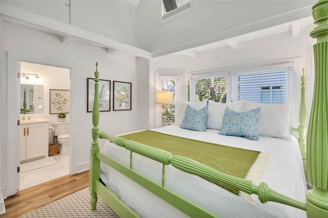 bedroom featuring beam ceiling, light hardwood / wood-style flooring, ensuite bath, and sink