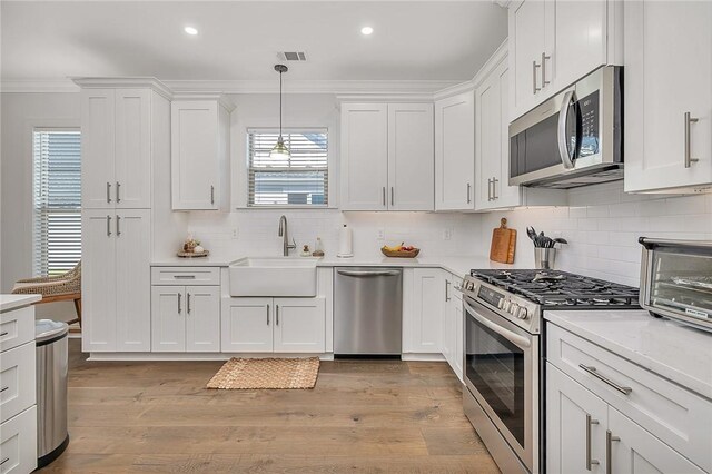 506 Conservation Dr, Saint Simons Island, GA 31522 - kitchen featuring stainless steel appliances, a sink, crown molding, light countertops, and white cabinetry