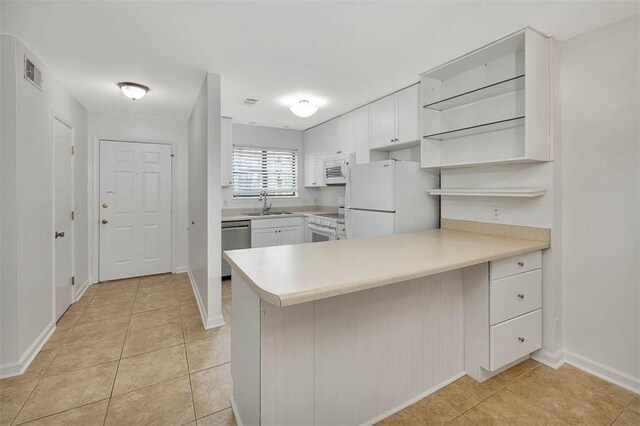 kitchen featuring sink, light tile patterned flooring, kitchen peninsula, white appliances, and white cabinets