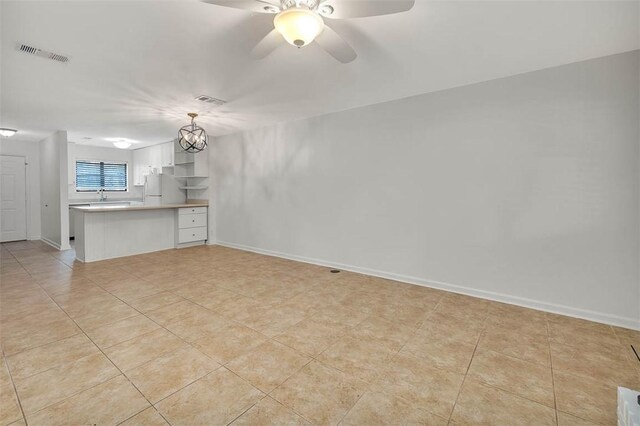 unfurnished living room featuring sink, light tile patterned flooring, and ceiling fan with notable chandelier