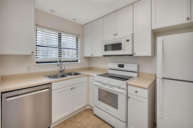 kitchen with white cabinetry, sink, light tile patterned floors, and white appliances