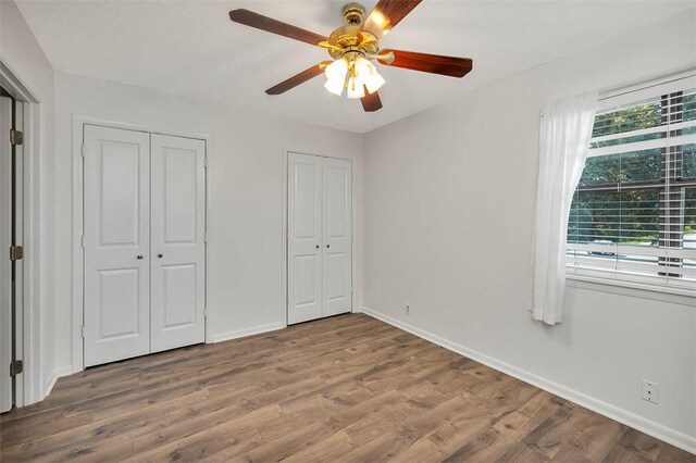 unfurnished bedroom with ceiling fan, wood-type flooring, and two closets