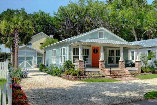 605 Ocean Blvd, Saint Simons Island, GA 31522 - view of front of home with covered porch, an outbuilding, gravel driveway, a metal roof, and a garage