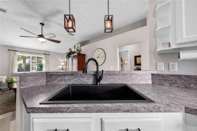 kitchen with white cabinets, sink, ceiling fan, a textured ceiling, and decorative light fixtures