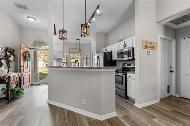 kitchen with white cabinets, stainless steel appliances, hanging light fixtures, and light hardwood / wood-style floors