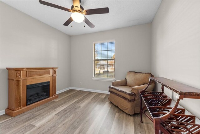 living area with ceiling fan, a textured ceiling, and light wood-type flooring