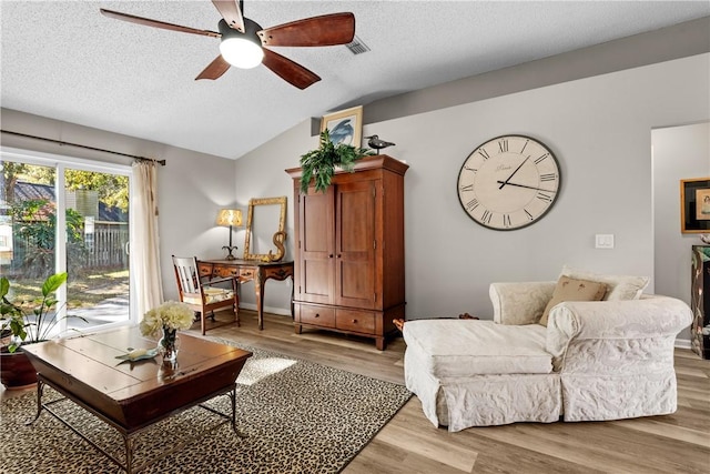 living room with ceiling fan, light hardwood / wood-style floors, a textured ceiling, and vaulted ceiling