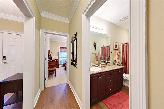 bathroom with ornamental molding, a textured ceiling, vanity, hardwood / wood-style flooring, and toilet