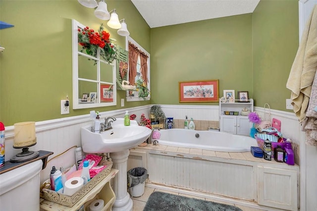 bathroom with a bath, toilet, tile patterned flooring, and a wainscoted wall