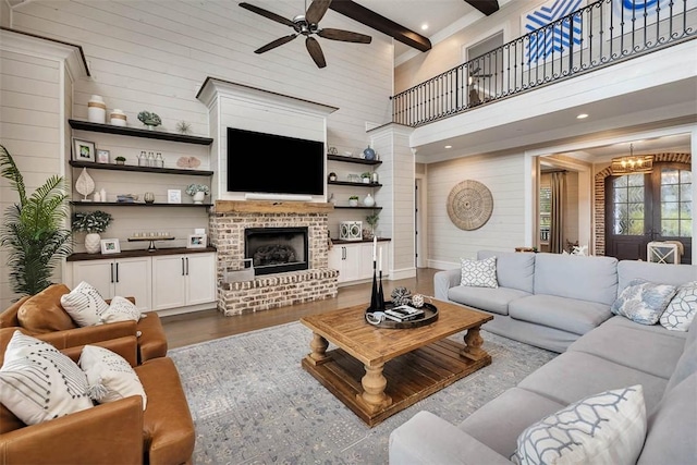 living room featuring dark wood-type flooring, a high ceiling, a fireplace, beam ceiling, and ceiling fan with notable chandelier