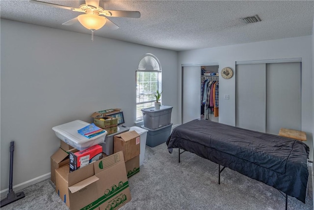 bedroom with multiple closets, ceiling fan, light carpet, and a textured ceiling