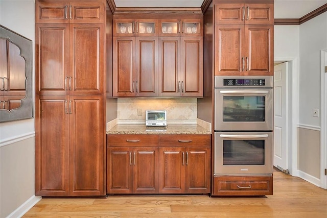 213 Five Pounds Rd, Saint Simons Island, GA 31522 - kitchen with stainless steel double oven, light stone countertops, baseboards, light wood-style flooring, and crown molding