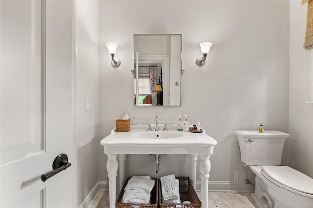 half bath with baseboards, a sink, and toilet