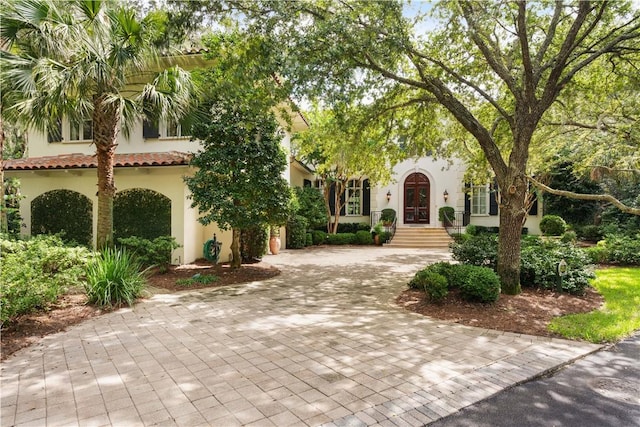 mediterranean / spanish house with french doors, decorative driveway, a tile roof, and stucco siding