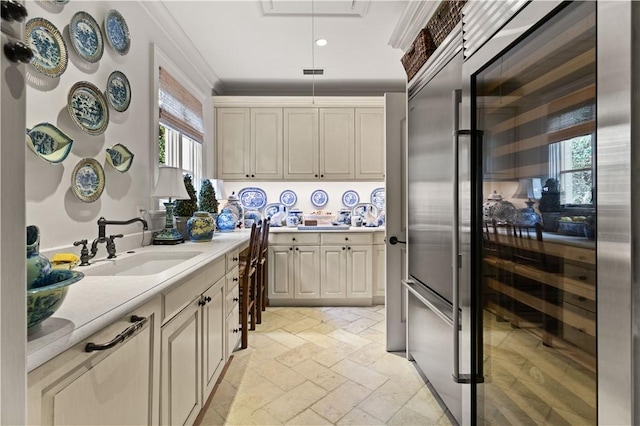 kitchen with pendant lighting, stone tile floors, light countertops, ornamental molding, and a sink