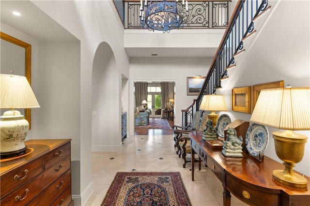 foyer entrance with baseboards, a towering ceiling, stairs, a notable chandelier, and light tile patterned flooring