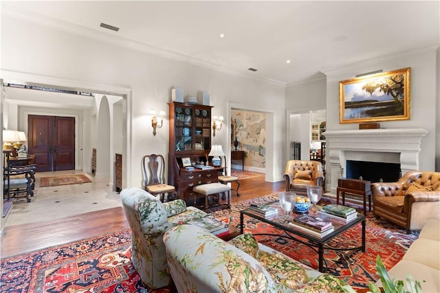 living room featuring a fireplace, wood finished floors, visible vents, baseboards, and ornamental molding