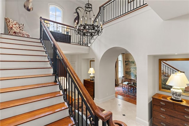 stairway featuring a towering ceiling, baseboards, a chandelier, and arched walkways