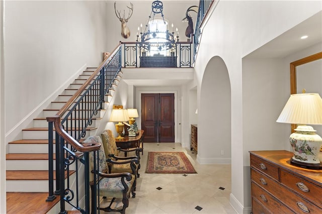 foyer entrance with baseboards, arched walkways, a towering ceiling, stairway, and a notable chandelier