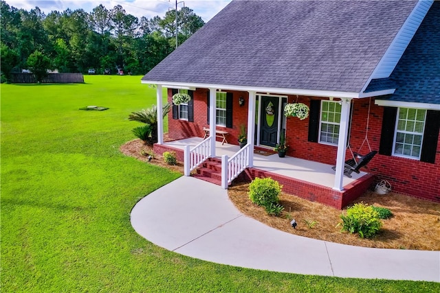 view of front of home with brick siding, roof with shingles, covered porch, and a front yard