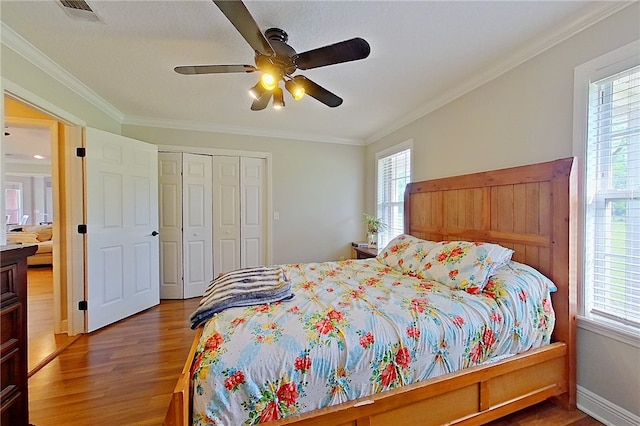 bedroom featuring crown molding, visible vents, multiple windows, and wood finished floors