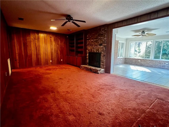 unfurnished living room featuring wooden walls, carpet, a textured ceiling, and a brick fireplace