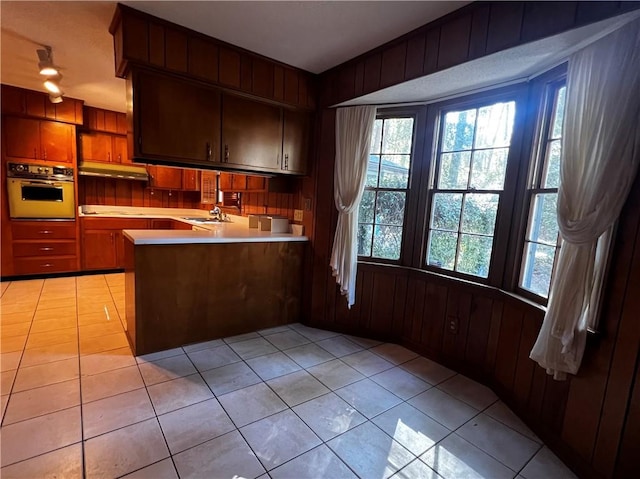 kitchen featuring oven, sink, wooden walls, light tile patterned floors, and kitchen peninsula