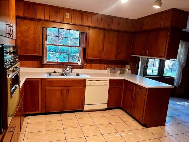 kitchen featuring stainless steel oven, white dishwasher, sink, light tile patterned floors, and kitchen peninsula