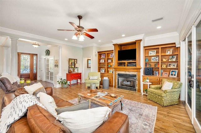 living room with decorative columns, crown molding, ceiling fan, and light wood-type flooring