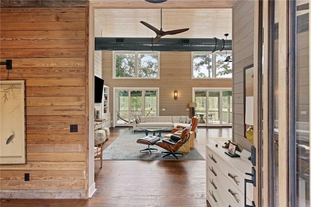 living room with wooden walls, dark hardwood / wood-style flooring, ceiling fan, and a high ceiling