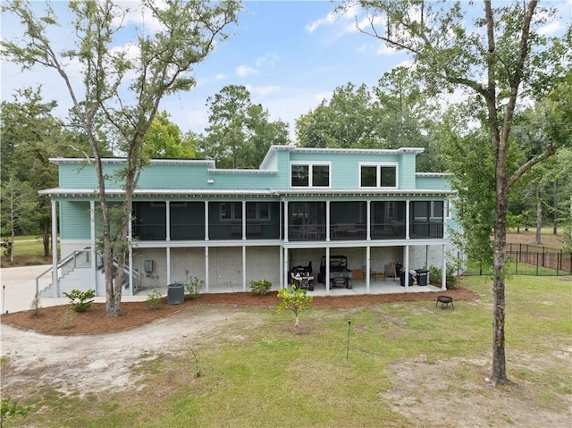 rear view of property with central AC unit, an outdoor fire pit, a sunroom, a patio, and a lawn