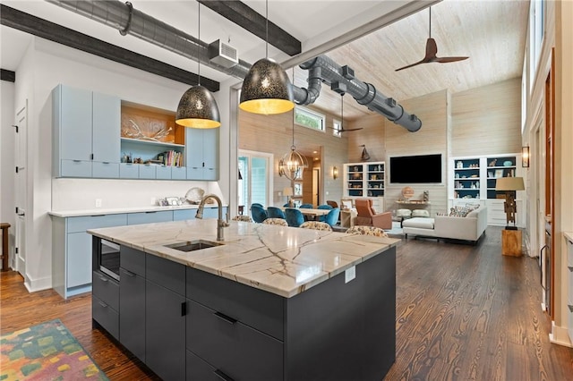 kitchen featuring sink, dark wood-type flooring, an island with sink, pendant lighting, and ceiling fan with notable chandelier