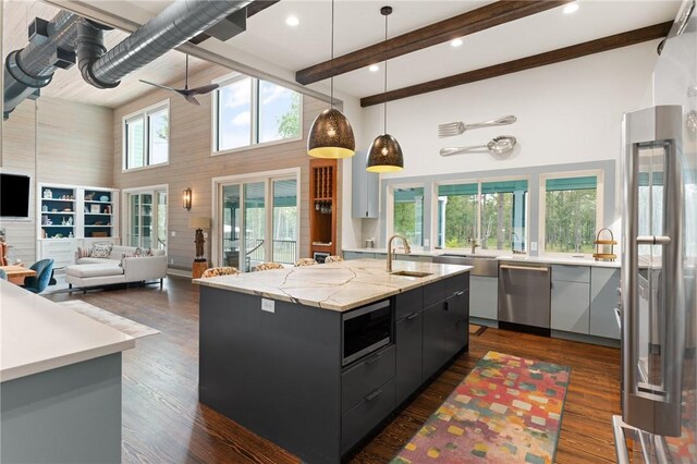 kitchen featuring ceiling fan, high vaulted ceiling, decorative light fixtures, a center island with sink, and appliances with stainless steel finishes