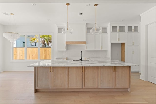 kitchen featuring light stone countertops, a large island, light wood-type flooring, white cabinetry, and a sink
