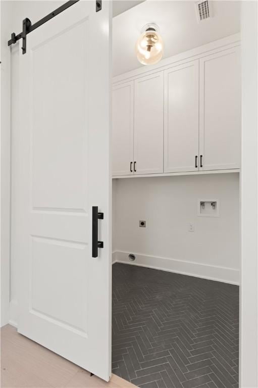 laundry area featuring cabinet space, a barn door, baseboards, hookup for an electric dryer, and visible vents