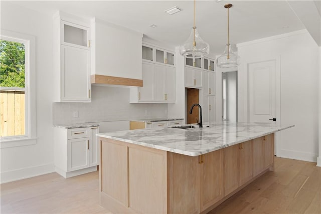 kitchen featuring a sink, light wood-type flooring, a large island with sink, and light stone countertops