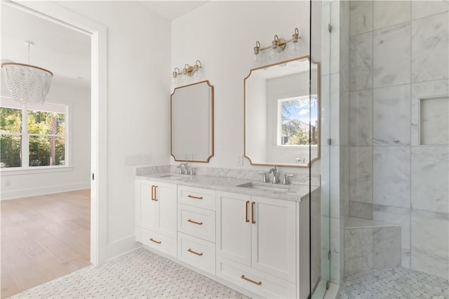 bathroom with a sink, an inviting chandelier, double vanity, and a shower