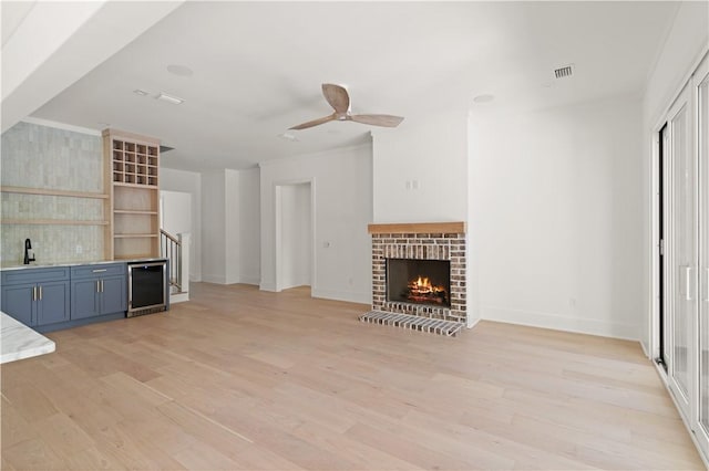 unfurnished living room featuring light wood-style floors, a sink, visible vents, and beverage cooler