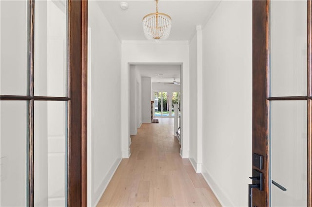 corridor featuring crown molding, baseboards, light wood-style flooring, and a chandelier