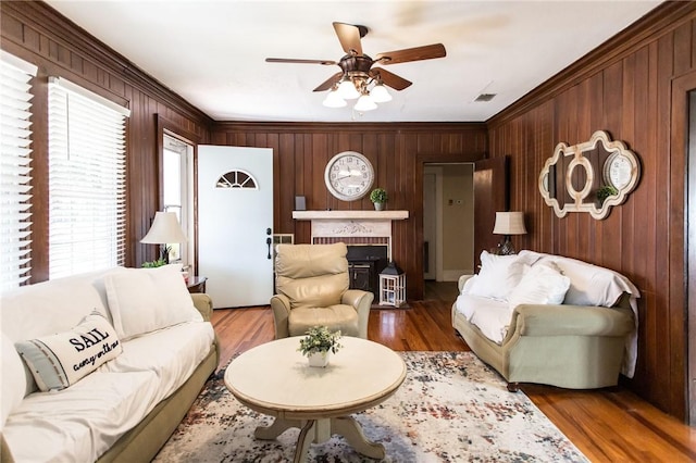 living room featuring hardwood / wood-style floors, wood walls, crown molding, a brick fireplace, and ceiling fan