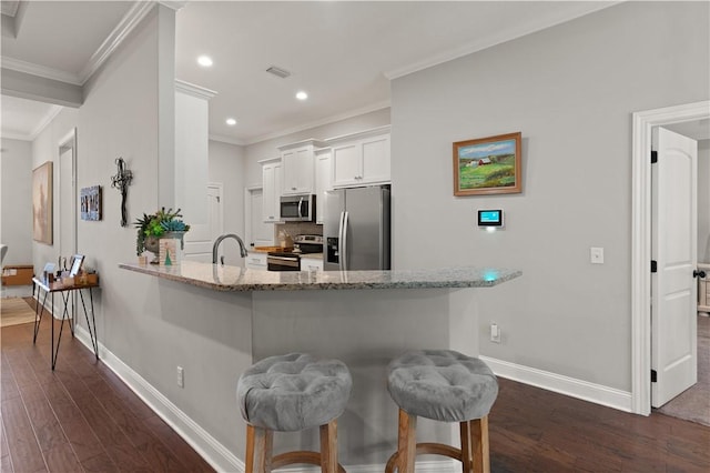 kitchen with a kitchen bar, light stone counters, stainless steel appliances, crown molding, and white cabinets