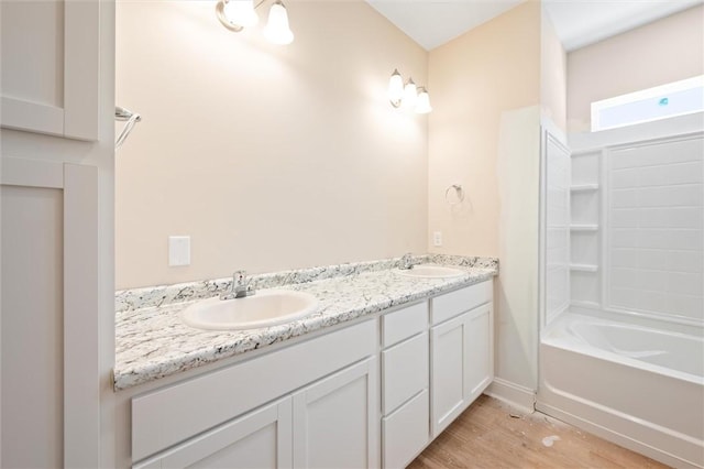 full bath with double vanity, a sink, baseboards, and wood finished floors