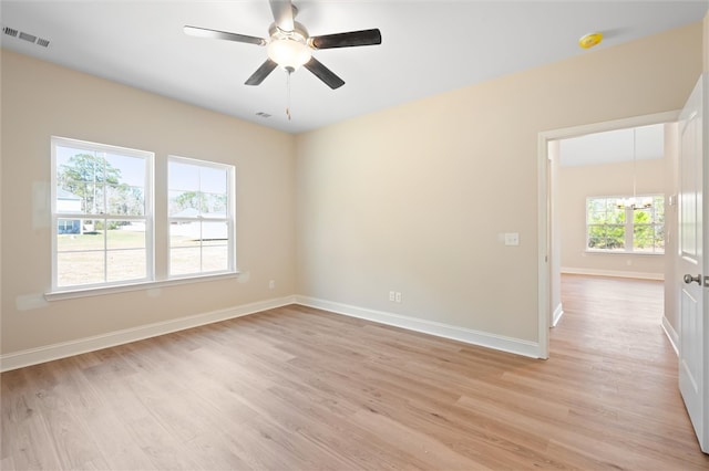 spare room featuring light wood-style floors, baseboards, visible vents, and ceiling fan with notable chandelier