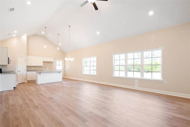 unfurnished living room featuring high vaulted ceiling, light wood-style flooring, ceiling fan with notable chandelier, a sink, and visible vents