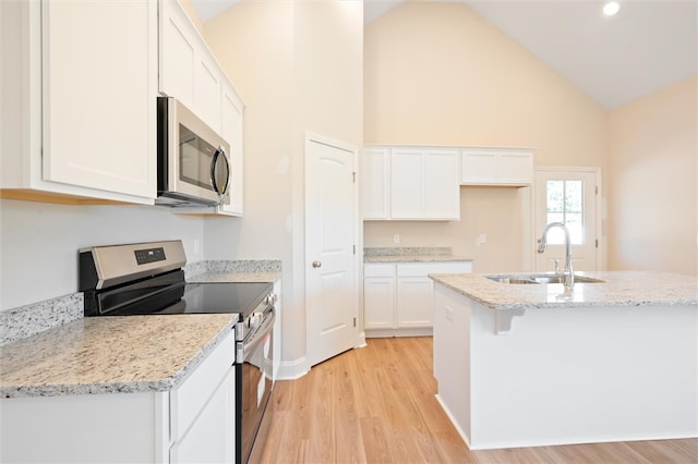 kitchen with stainless steel appliances, a sink, white cabinetry, light wood-type flooring, and a center island with sink