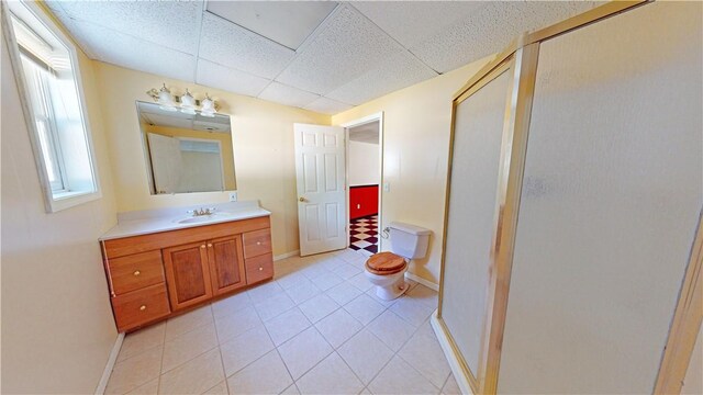 bathroom with a drop ceiling, tile patterned floors, toilet, a shower with door, and vanity